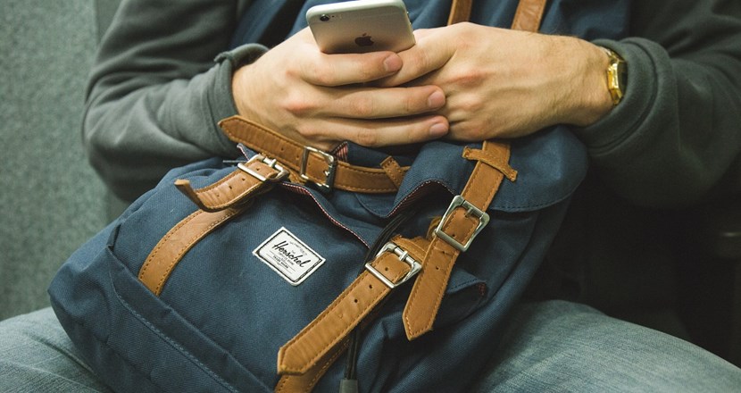 Två händer på en ryggsäck som håller i en mobiltelefon