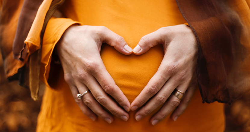 Händer som formar ett hjärta på gravid kvinnas mage. Foto. 