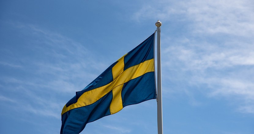 Svenska flaggan fladdrar blå-gul mot en blå himmel.