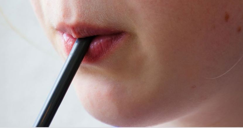 Närbild på mun som blåser ut luft genom sugrör