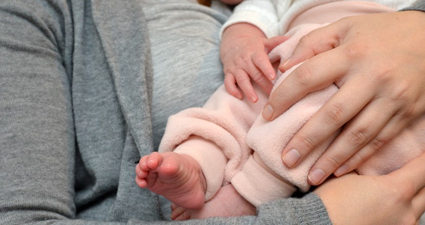 Närbild på person som håller ett spädbarn i famnen. Foto.