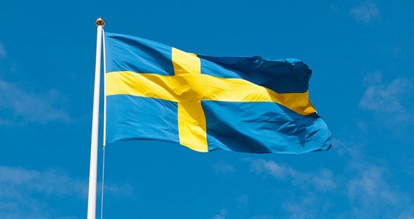 Foto på en svensk flagga, som fladdrar i vinden, med en blå himmel som bakgrund.
