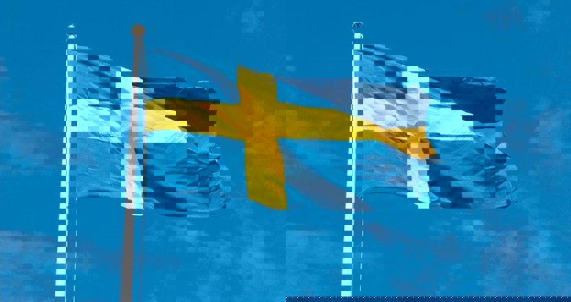Foto på en svensk flagga, som fladdrar i vinden, med en blå himmel som bakgrund.