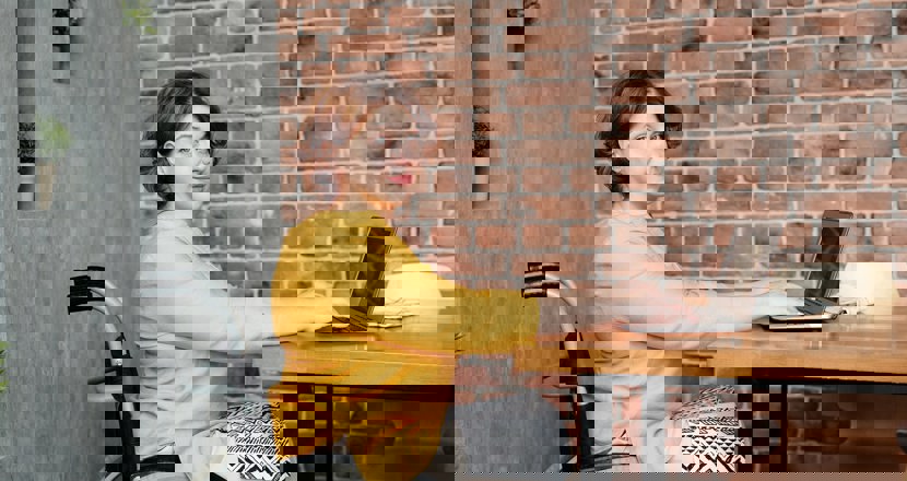 Kvinna i rullstol sitter vid ett bord med sin bärbara dator.