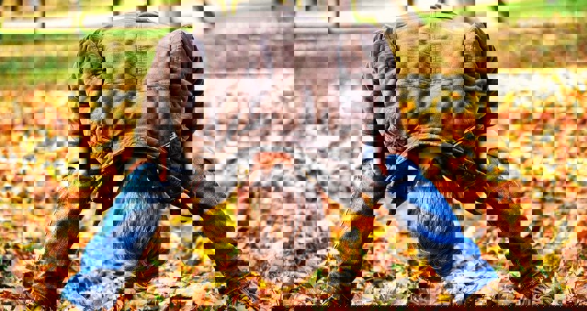 Ett barn som står bredbent och böjer ner huvudet mellan knäna. Foto.