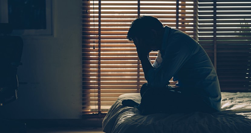 En person sitter i mörkret bakom en persienn. Foto: istockphoto.