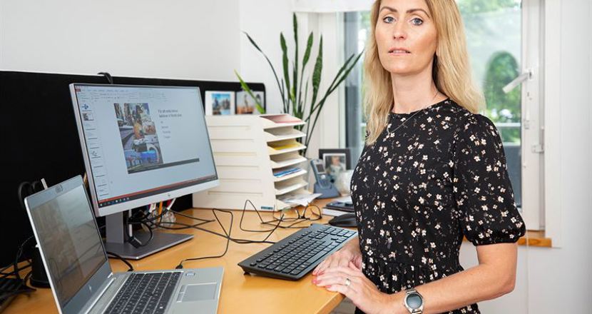 Charlotte Wassenius står vid sin dator vid sitt skrivbord. Foto.
