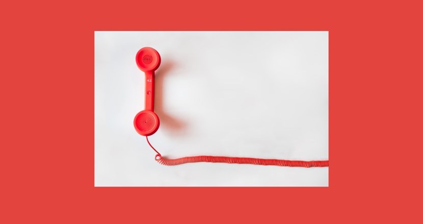 En röd telefonlur med telefonsladd mot en enfärgad ljusgrå bakgrund.