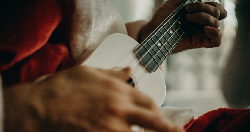 Närbild på tomteklädd man som spelar på lite gitarr, man ser bara instrumentet och händerna.