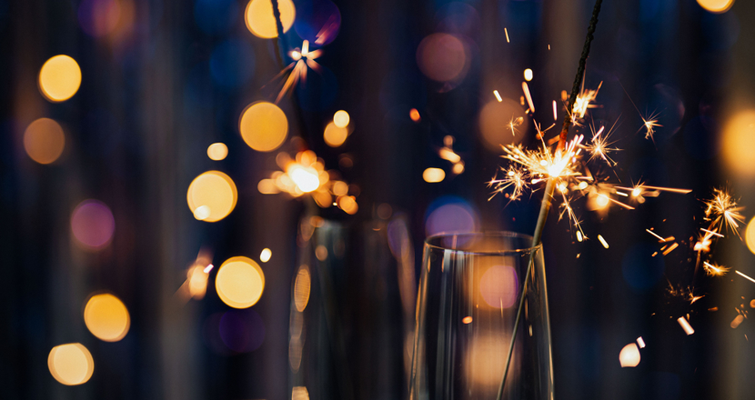 Champagneglas med sprakande tomtebloss i närbild mot en gnistrande blå bakgrund.