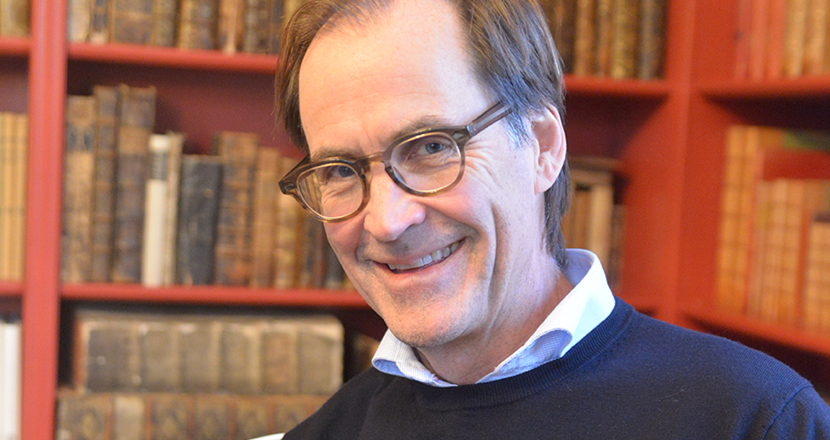 Porträttbild på Jan Hillert framför en bokhylla. Foto.