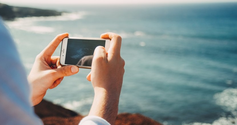 En person som sitter vid havet med sin mobiltelefon. Foto.