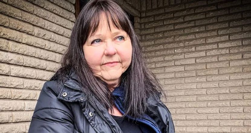 Annika sitter i svart jacka utanför sitt hus med sandstensfärgat tegel. Hon har mörkt halvlångt hår med lite lugg.