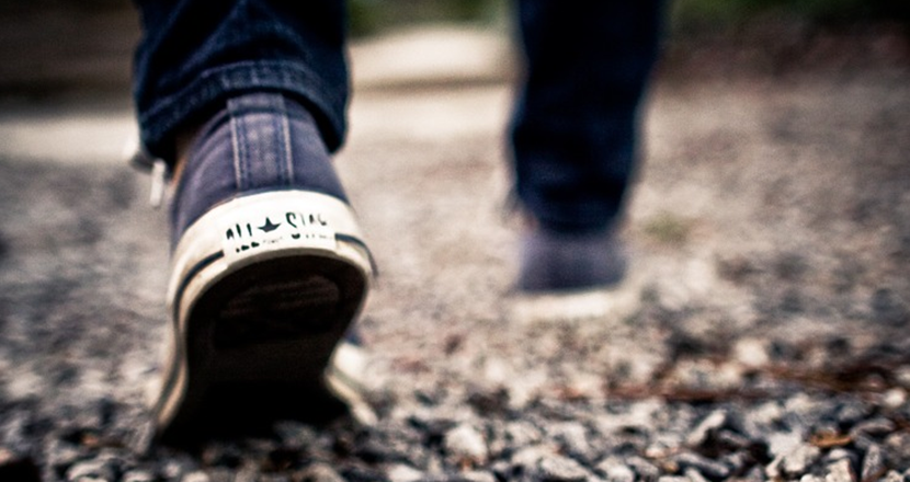 Bild på ett par mjuka skor som går på grovt grus, bilden är lite oskarp och kan förmedla känsla att gå med smärta.