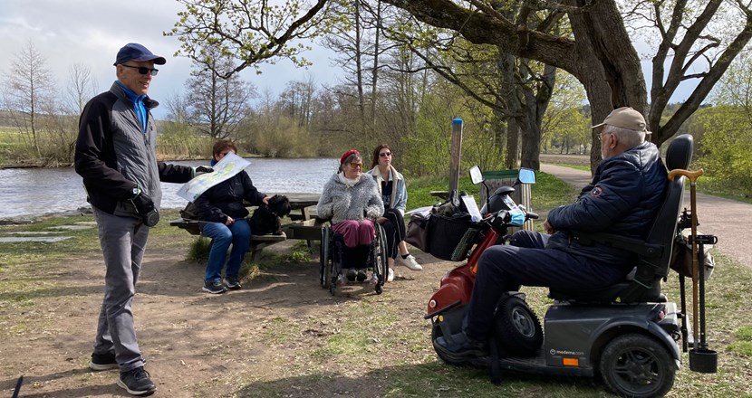 Bild på en grupp människor med rullstol och elskoter som har picknick vid Fyrisån i maj.