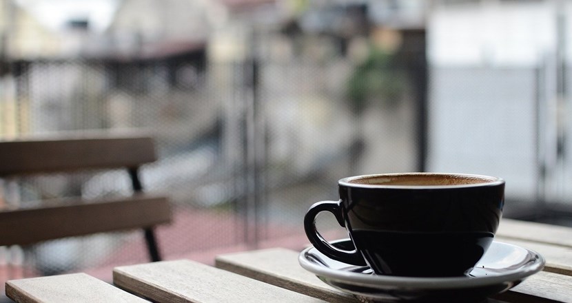 En svart kaffekopp står på ett bord med en suddig bakgrund. Foto.