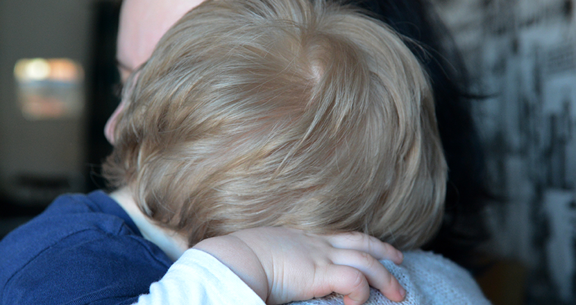 Ett litet barn som sover på en vuxen axel. Foto.