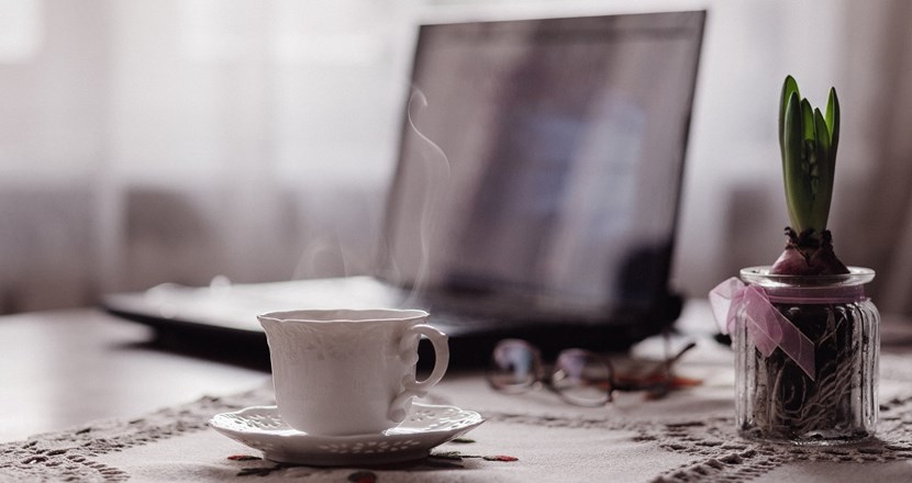 En rykande varm kopp kaffe i en fin vit kopp med en dator i bakgrunden