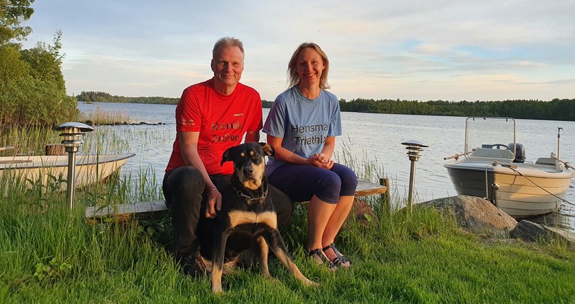 Lennart och Eva på en bänk vid en sjö tillsammans med en stor hund. Foto.