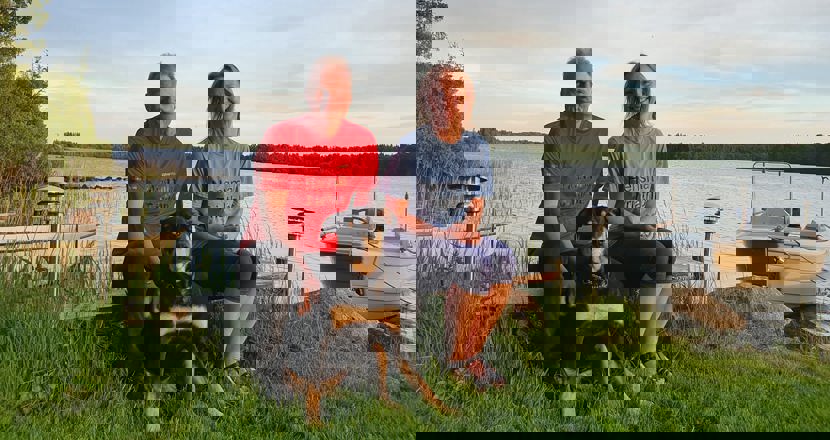 Lennart och Eva på en bänk vid en sjö tillsammans med en stor hund. Foto.