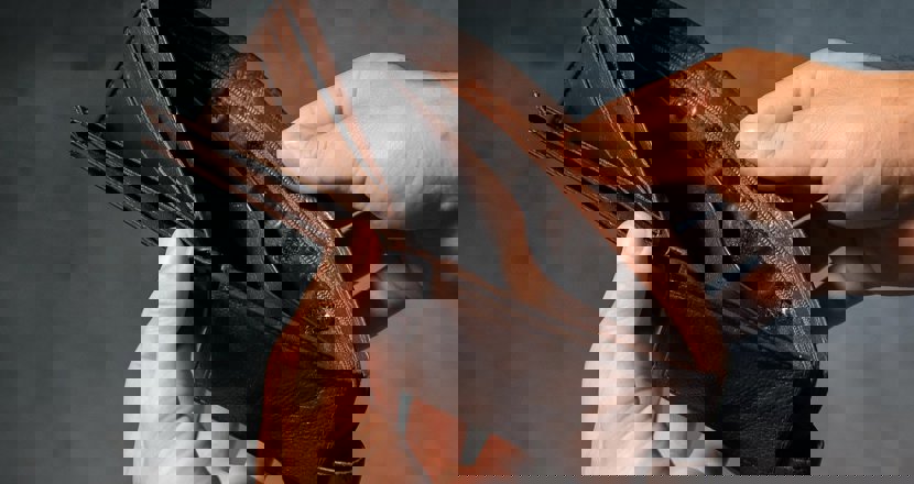 En tom brun plånbok som hålls upp av två händer. Foto.