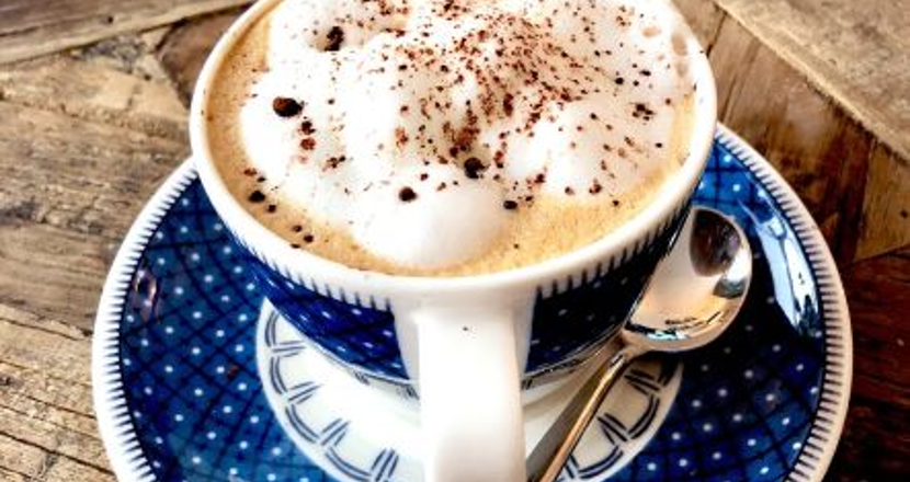 En kopp cappucino i en blå- och vitmönstrad kopp med fat som står påträyta. Foto.