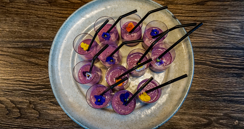 Små glas med lila innehåll och svarta sugrör. Foto.