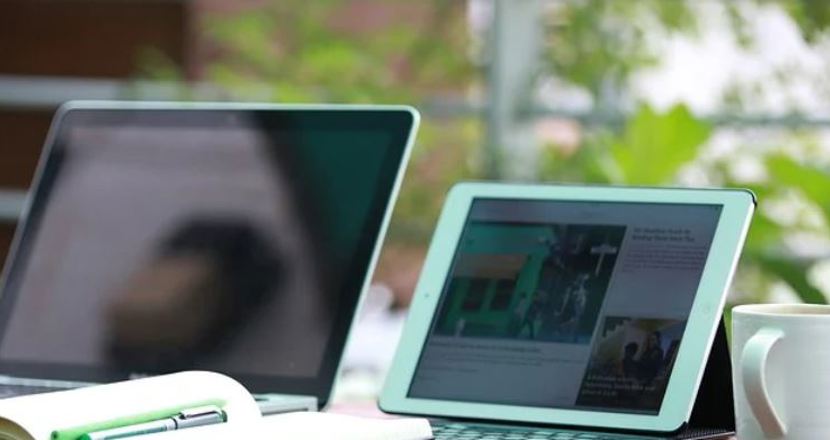 Läsplatta och pc på bord vid ett fönster med en kaffekopp på bordet.