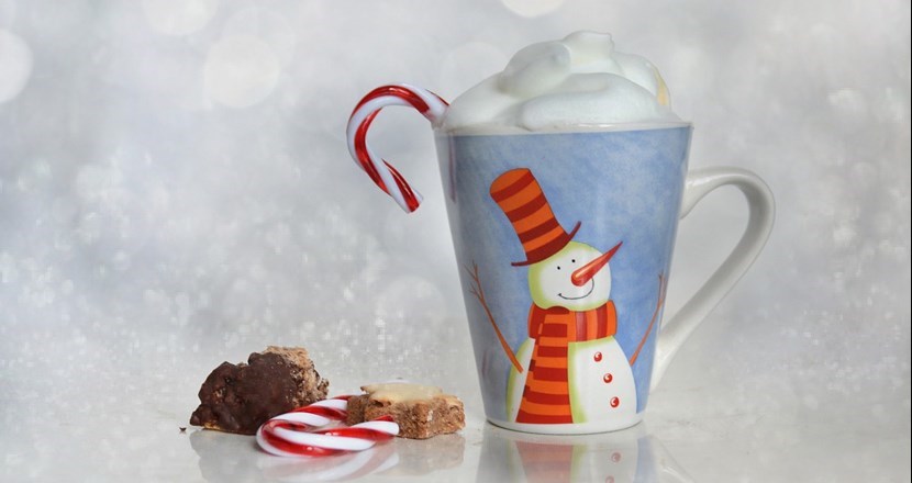 En mugg med en snögubbe på, med något som ser ut som varm choklad med vispgrädde. Till höger ligger lite julgodis. Foto.