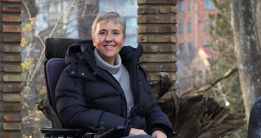 Lise Lidbäck i sin rullstol mot en höstlik bakgrund. Foto.