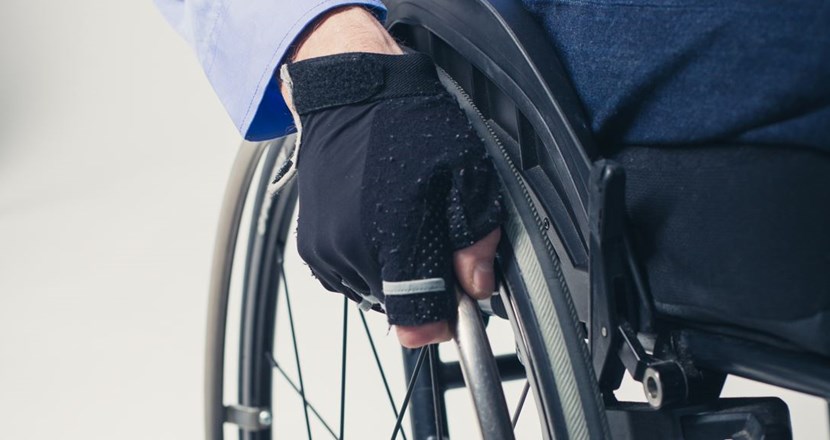 Närbild på ett rullstolshjul med en person i rullstolen som har en hand på hjulet. Foto.