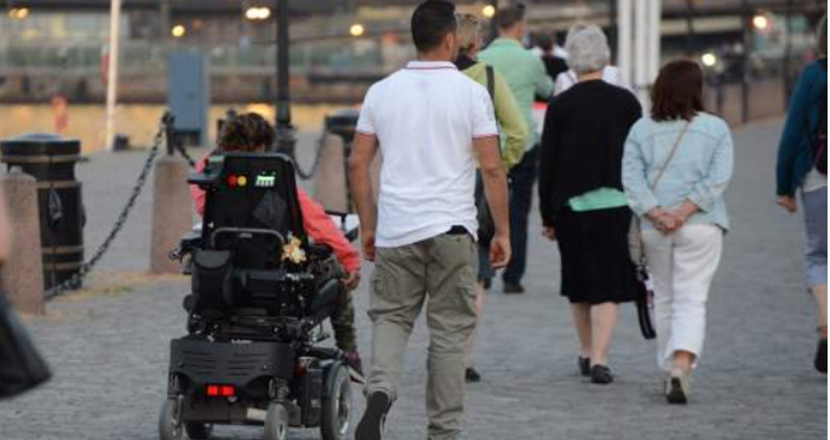 Två personer, en gående och en i rullstol. Foto.