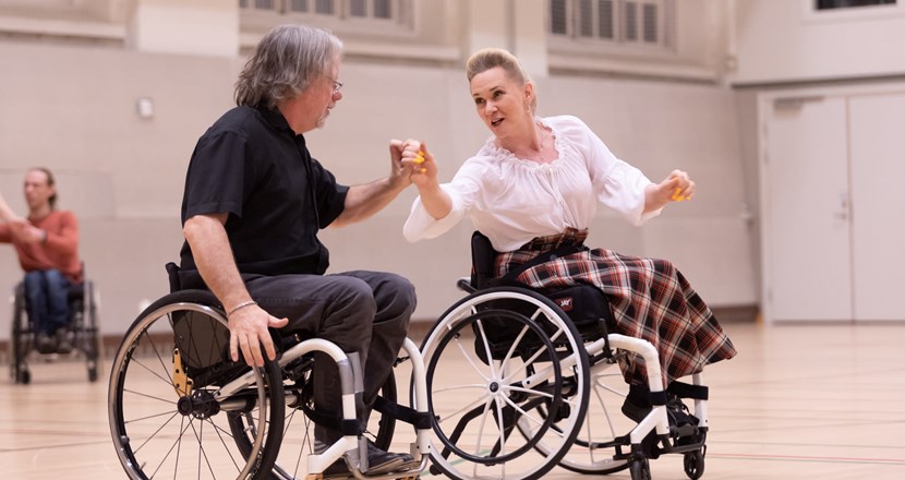 Två personer i varsin rullstol, på dansgolvet i en idrottshall. Foto.