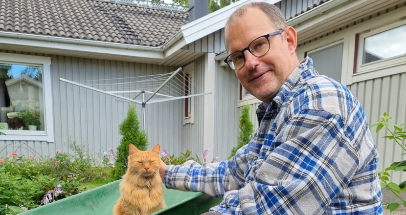 Krister sitter på huk vid en skottkärra med en katt i. Foto.