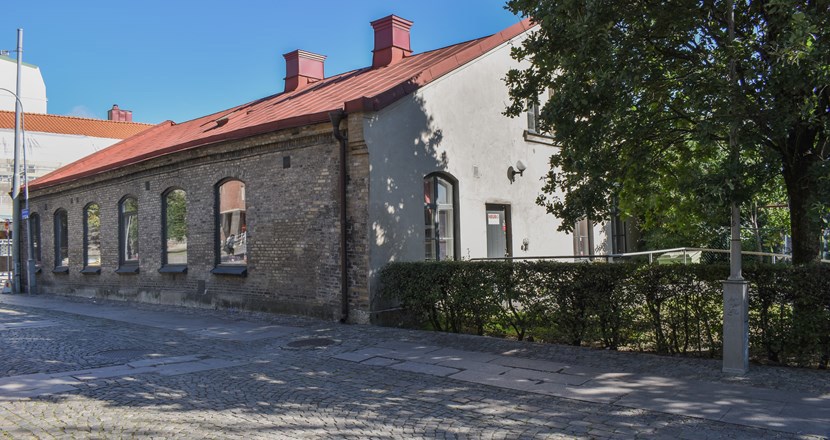 Fasaden på en äldre brunbeige tegelbyggnad vid en kullerstensgata. Foto.