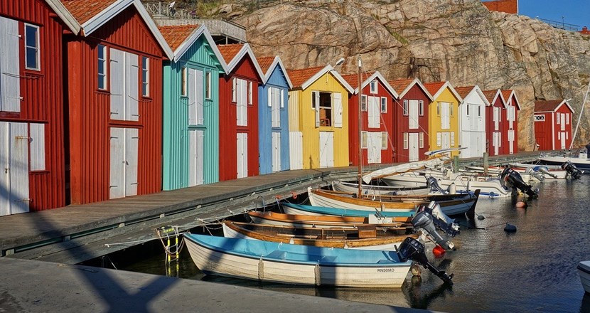 Bilden visar en brygga med färgglada fiskebodar och ankrade småbåtar.
