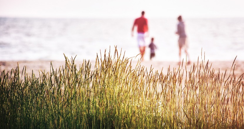En man, ett barn och en kvinna syns på långt håll vid en strand. Foto.
