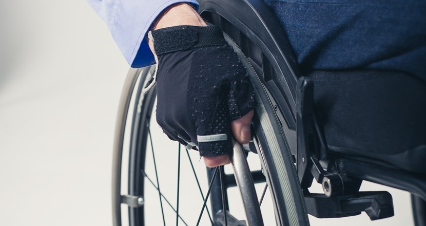 Närbild på ett rullstolshjul, en person med handen på hjulet. Foto.