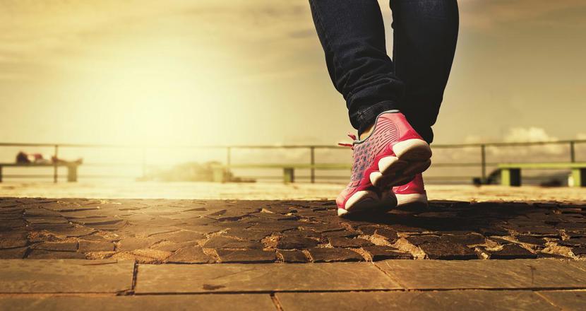 Ben och fötter som går bortåt mot solnedgången. Foto.