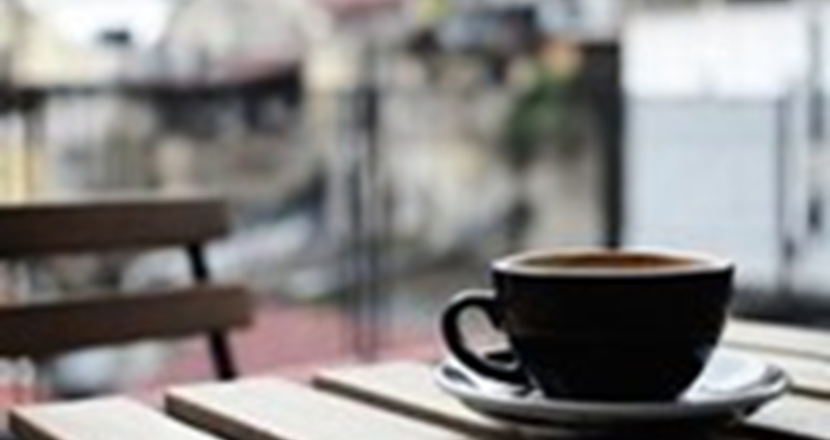 En svart kaffekopp står på ett bord i trä. Foto.