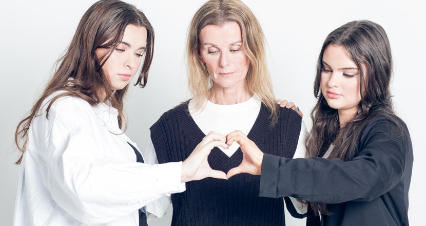 Tre kvinnor. Två som stöttar kvinnan i mitten. Foto.