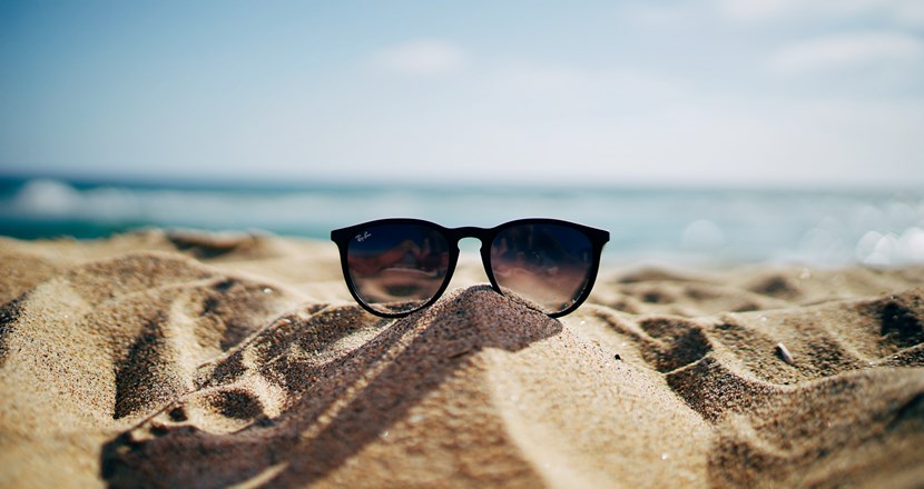 Solglasögon på en strand med havet i bakgrunden. Det ser ut att vara en solig sommardag.