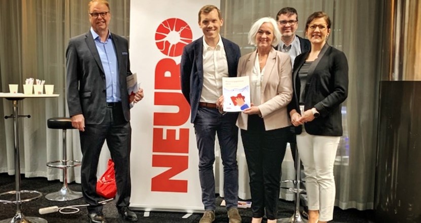 Ett antal människor som står framför och håller fram årets Neurorapport. Foto.