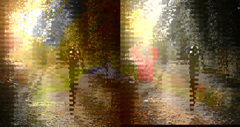 Kvinna är ute och går i skogen i solnedgången