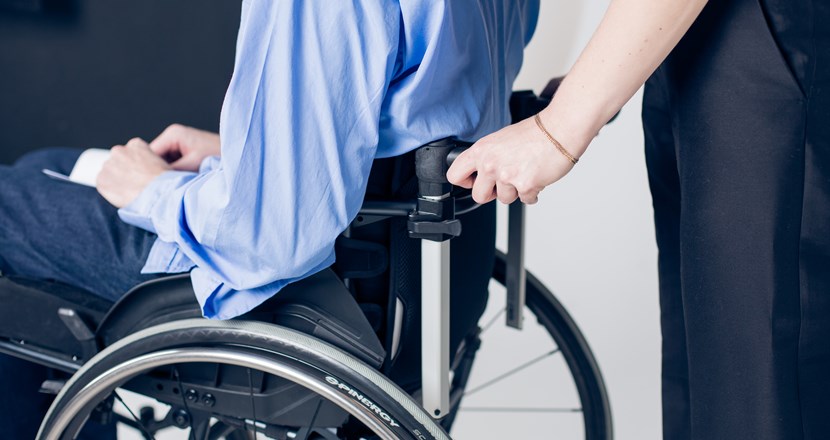 Närbild på en person i manuell rullstol som körs av en medhjälpare. Foto.