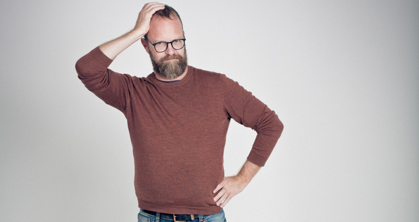 En man som har ena handen i midjan och kliar sig i huvudet med den andra. Foto.