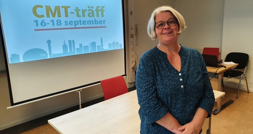 Carina står framför en Powerpoint på stor duk. Hon har kort ljust hår, glasögon och en blågrön blus