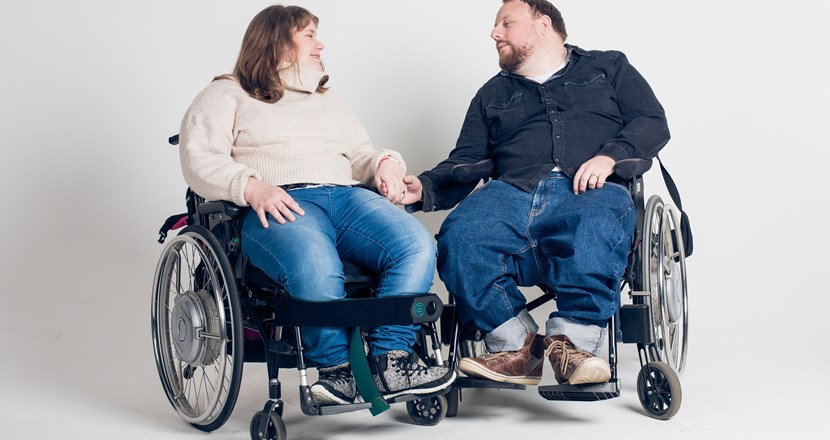 Två glada personer i varsin rullstol. Foto.