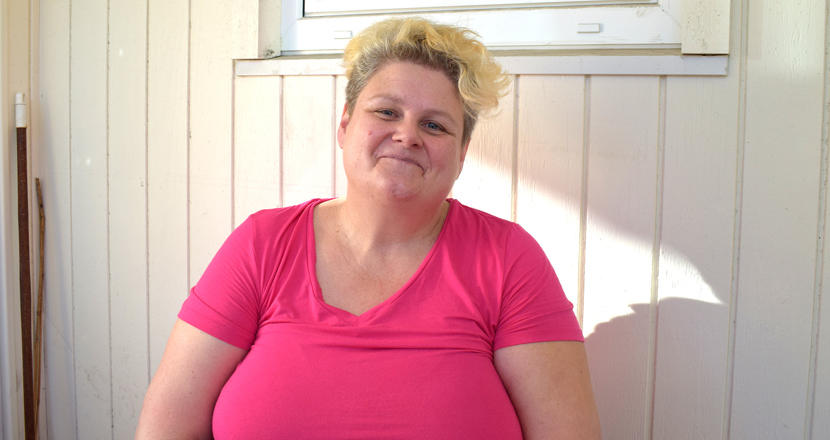 Ulrika i rosa topp framför en ljusbeige träpanel. Foto.