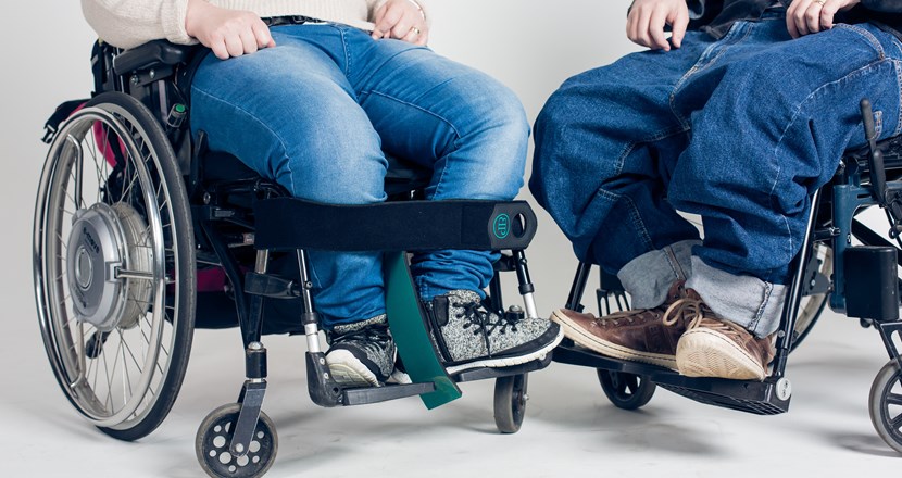 Närbild på två personers ben, de sitter i varsin rullstol. Foto.